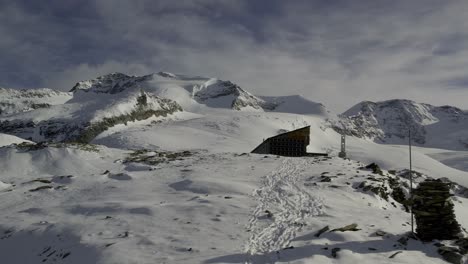 Drone-approaches-Rifugio-Quintino-Sella-al-Felik,-revealing-the-impressive-backdrop-of-Castore-and-Lyskamm-peaks-adorned-with-glaciers-in-the-stunning-alpine-landscape