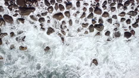 Vista-De-Fondo-De-Arriba-Hacia-Abajo-De-Las-Olas-De-Espuma-Salpicando-En-La-Costa-Rocosa-De-Guijarros,-Tenerife