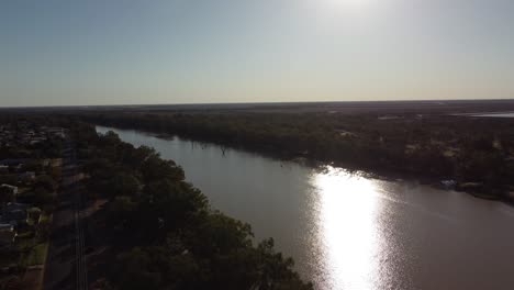 Drone-approaching-a-river-at-sunset-country-town-on-the-left-side