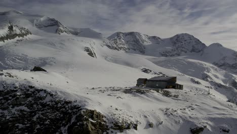 Dynamic-drone-tracking-shot-of-Rifugio-Quintino-Sella-al-Felik,-showcasing-the-mountain-refuge-against-the-stunning-backdrop-of-the-Monte-Rosa-Massiv