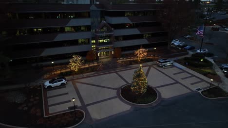 Toma-Aérea-Acercándose-A-Un-Edificio-De-Negocios-En-Greenfield-Lancaster-Con-árboles-Iluminados-Decorados-Al-Atardecer