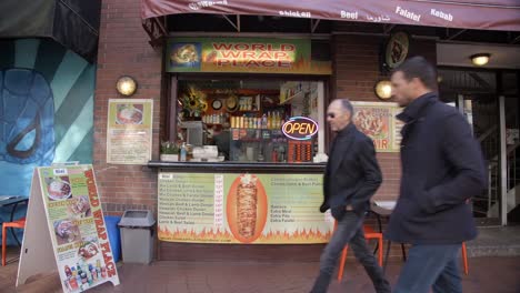 Individuals-Walking-Past-a-Food-Kiosk-in-Vancouver,-Canada---Handheld-Shot