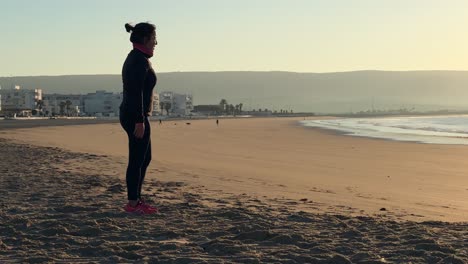 Im-Sanften-Schein-Des-Tiefstehenden-Sonnenlichts-Strahlt-Eine-Frau-Vitalität-Aus,-Während-Sie-Am-Meeresstrand-Mit-Sprüngen-Und-Hüftübungen-Trainiert-Und-So-Die-Essenz-Von-Fitness-Und-Erholung-Verkörpert