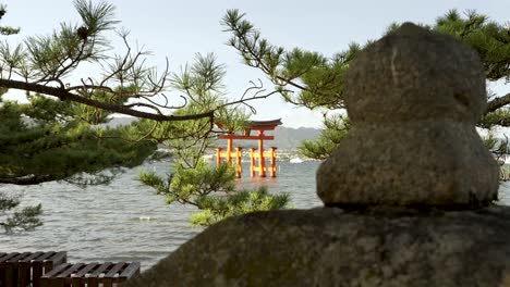 Puerta-Flotante-Grand-Torii-Durante-La-Puesta-De-Sol-En-El-Fondo-En-Itsukushima-Vista-A-Través-De-Ramas-De-Pinos-En-Primer-Plano