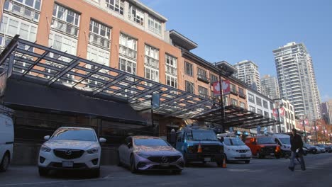 Vancouver,-Canadá---Calle-Continental-En-Yaletown-Con-Un-Hombre-Caminando-Junto-A-Una-Fila-De-Autos-Estacionados,-Detrás-Hay-Un-Hombre-En-Bicicleta---Toma-Estática