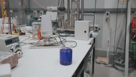 Zoom-Lento-En-Un-Líquido-Azul-En-Un-Vaso-De-Precipitados-Que-Descansa-Sobre-Una-Mesa-En-Un-Laboratorio