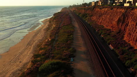 Toma-Aérea-Rastrea-A-Un-Ciclista-Cabalgando-Por-Los-Acantilados-En-Del-Mar,-Ca-Al-Atardecer