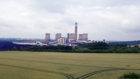 Low-Level-Drohnenaufnahmen-Von-Rechts-Nach-Links-Schwenken-über-Ackerland-Mit-Einem-Kohlekraftwerk-Als-Mittelpunkt-Des-Interesses