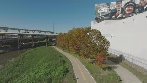 An-aerial-view-shows-a-male-cyclist-descending-while-another-male-cyclist-stands-to-pedal-up-a-short-climb-along-White-Oak-Bayou-in-Houston,-Texas