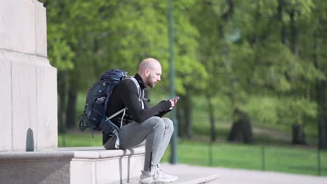 Person-sitting-on-steps-in-front-of-horse-statue-texting-with-his-phone-at-the-Royal-Palace-in-Oslo,-Norway