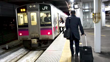 A-business-man-walking-towards-small-train-stopped-at-the-station-in-Aomori,-Japan