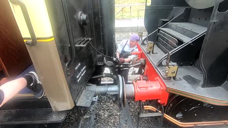 Man-uncoupling-steam-engine-from-carriages-at-station