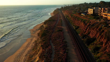 Aerial-shot-rises-above-cyclist-riding-along-the-bluffs-in-Del-Mar,-CA-at-sunset