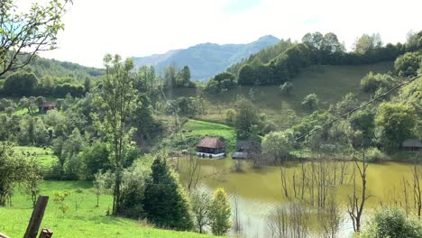 Vista-Al-Campo-En-Un-Pueblo-De-Rosia-Montana-Con-Antiguas-Casas-Rumanas-Tradicionales-Rodeadas-Por-Un-Lago-De-Barro-Y-Bosques-Verdes-En-Un-Día-Soleado-Y-Luminoso