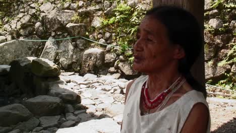 An-old-Ifugao-woman-is-talking-with-someone-while-she-sits-under-a-native-grass-hut-on-stilts-in-Bataad-Philippines