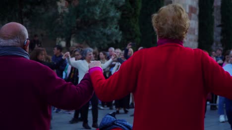 Toma-Panorámica,-Personas-Mayores-Cogidas-De-La-Mano-En-La-Danza-Tradicional-Sardana-En-Plaza-Nova,-Barcelona,-España,-Personas-Mayores-Al-Fondo