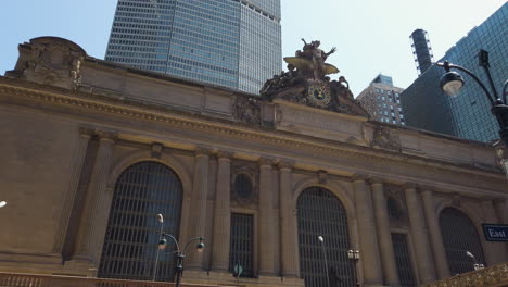 La-Gran-Estación-Central-De-Nueva-York-Filmada-Desde-Afuera-En-La-Acera-Con-Gente-Pasando,-Inclinándose-Hacia-Arriba-Hacia-El-Mecanismo-De-Relojería.