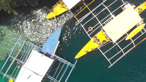 Aerial-rising-drone-shot-of-people-standing-on-a-Paraw-boat,-in-a-turquoise-lagoon,-in-between-limestone-cliffs,-on-a-sunny-day,-at-Coron-island,-Philippines,-Asia