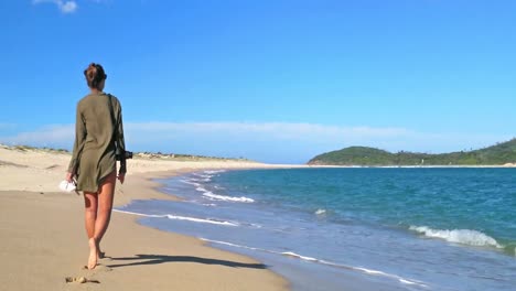 Schönes-Junges-Hipster-Mädchen,-Das-Herumläuft-Und-Sich-Umdreht,-Um-Mit-Der-Kamera-Auf-Den-Strand-Zurückzublicken