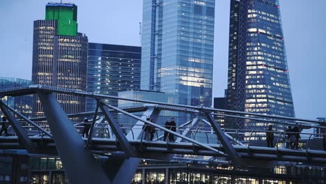 People-Walking-At-The-London-Millennium-Footbridge-In-London,-UK-With-Skyscrapers-In-The-Background---Midshot