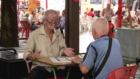 Two-old-men-light-up-a-cigarette-while-playing-Chinese-chess-in-Chinatown,-Singapore