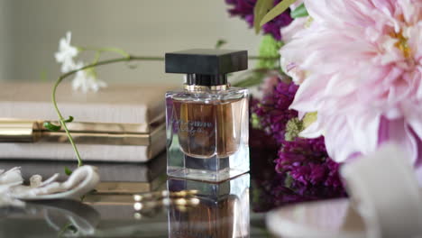 Glass-Perfume-Bottle-on-a-reflective-table-next-to-a-bouquet-of-pink-flowers