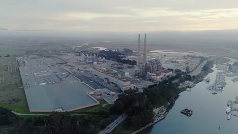 Toma-Aérea-En-órbita-Distante-De-Una-Planta-De-Energía-Y-Smog-Distante-Al-Atardecer