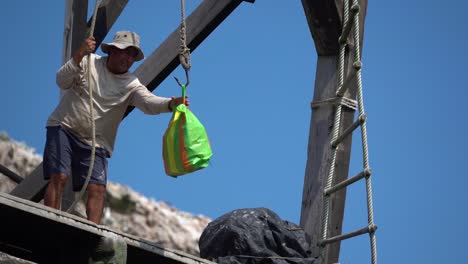 Hombre-Peruano-Levantando-Una-Colorida-Bolsa-De-Plástico-En-Un-Gancho-En-El-Puerto,-Cámara-Lenta