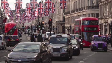 Buses-and-cars-are-passing-along-Regent-Street-in-the-summer-afternoon-in-the-rush-hour-in-London-while-the-camera-is-panning