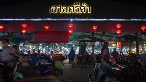 Shot-of-locals-entering-into-a-busy-local-market-across-the-road-in-Nan-province,-Thailand-at-night