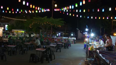 Toma-De-Puestos-De-Comida-Al-Borde-De-La-Carretera-Con-Muchos-Clientes-Disfrutando-De-La-Comida-En-La-Ciudad-De-Nan,-Tailandia,-Por-La-Noche