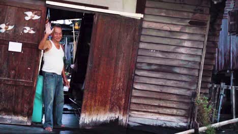 Sailing-Past-Local-Thai-Older-Male-Waving-From-Dilapidated-Canal-House