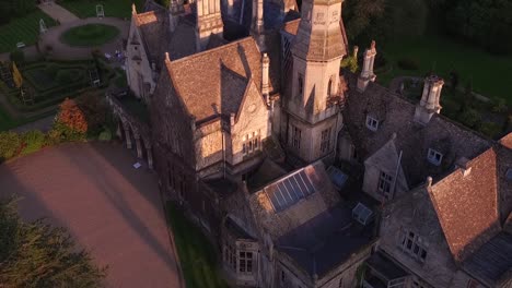 Toma-Aérea-De-La-Mansión-Junto-Al-Lago-Cheltenham-Gloucestershire-Revelación-De-La-Casa-Desde-El-Lago-En-La-Hermosa-Luz-Dorada-Del-Atardecer