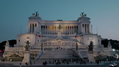 Aerial-view-over-traffic,-towards-the-Illuminated-Altar-of-the-Fatherland,-dusk-in-Rome,-Italy---tilt,-drone-shot