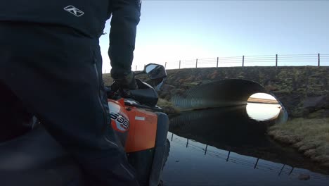 Vista-Detrás-Del-Ciclista-De-Un-Quad,-En-Una-Pista-Todoterreno-En-La-Naturaleza-Islandesa,-Cruzando-Un-Túnel-Inundado