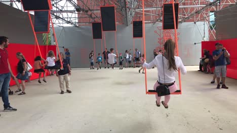 German-nursery-kids-swinging-on-long-swings-under-supervision,-wide-gimbal-shot