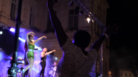 African-woman-from-the-audience-dancing-with-the-band-on-stage,-with-arms-raised