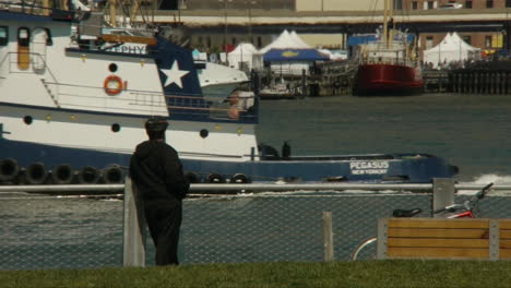 Man-watching-the-boats-pass-by-on-the-East-River-in-Brooklyn-and-joggers-run-by