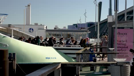 Passengers-disembark-public-GVB-ferry-in-sunny-Amsterdam,-side-slomo