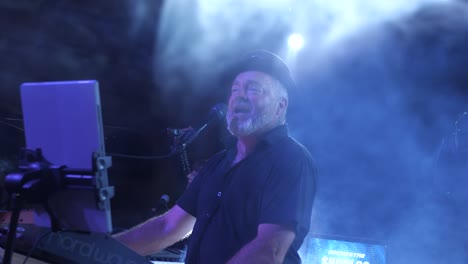 Cantante-Enérgico-De-Unos-Cincuenta-Años-Con-Sombrero,-Actuando-En-El-Escenario-Con-Humo-Y-Luces-Azules