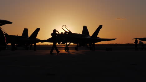 Eine-Breitere-Silhouettenaufnahme-Eines-Marineoffiziers,-Der-Vor-Einem-Blauen-Engel-Auf-Dem-Rollfeld-Läuft,-Während-Die-Jets-Für-Eine-Flugshow-Am-Frühen-Morgen-Bei-Sonnenaufgang-In-Key-West-Vorbereitet-Werden