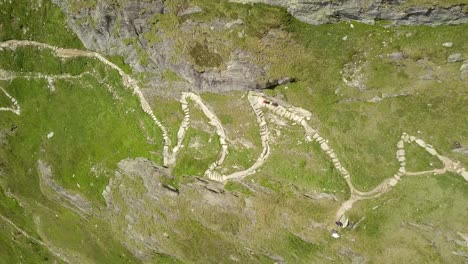 Zoom-Aéreo-Sobre-Dos-Excursionistas-En-Un-Empinado-Sendero-De-Montaña-En-Zigzag