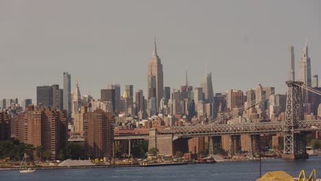 Plano-Panorámico-Del-Río-Este,-El-Puente-De-Manhattan-Y-El-Horizonte-Con-El-Edificio-Empire-State-Al-Fondo-Al-Atardecer