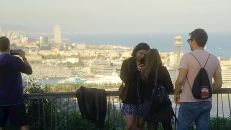 People-on-viewpoint-overlooking-city-and-harbor-and-taking-photos-with-smartphone-during-sunset