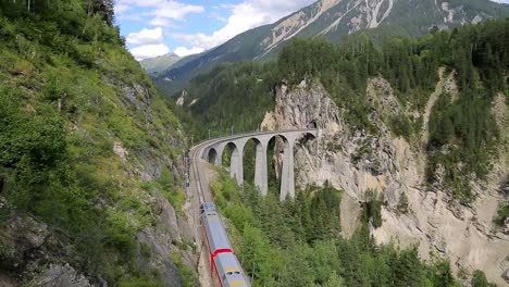 Swiss-train-travels-along-epic-arched-viaduct-bridge-in-Alps-mountains