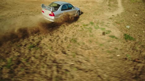 FPV-Renndrohne-Jagt-Einen-Stunt-Autofahrer,-Der-Auf-Einem-Unbefestigten-Fußballfeld-Tricks-Vorführt