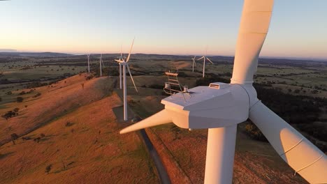 Wind-turbine-spins-in-the-golden-light-of-the-rising-sun,-The-wind-farm-can-be-seen-behind-the-large,-golden-blades