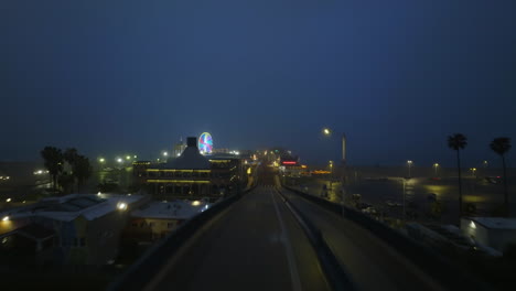 Drone-shot-through-the-gate-toward-the-Santa-Monica-pier,-foggy-night-in-LA,-USA