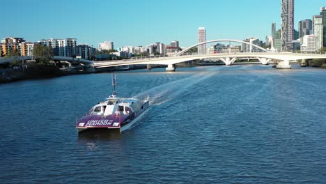 Disparo-De-Drone-Rastreando-El-Barco-Gato-De-La-Ciudad-En-El-Río-Brisbane,-Mirando-Hacia-La-Ciudad-De-Brisbane-Y-Los-Puentes