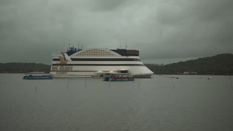 The-wide-view-shows-a-vivid-view-of-the-Mandovi-River-in-Goa,-India-with-colorful-casinos-on-a-cloudy-day,-creating-a-dramatic-and-vibrant-atmosphere